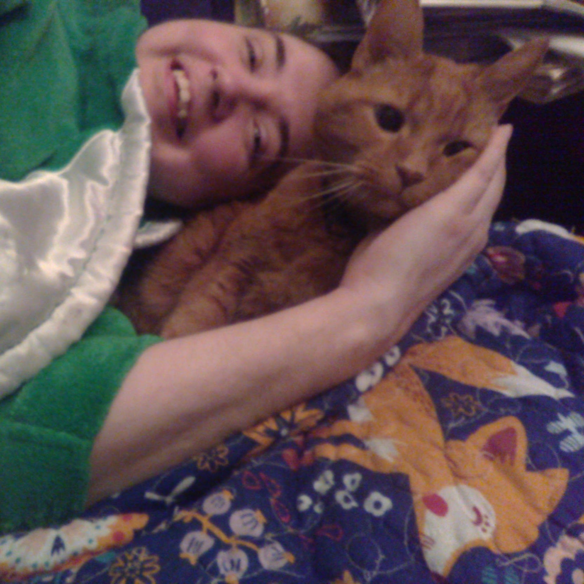 Portrait haut du corps de Clément le chat et moi couchés sur le canapé sur notre couverture préférée la bleue avec des renards. Je suis couchée la tête contre Clément et ma main tient sa tête.