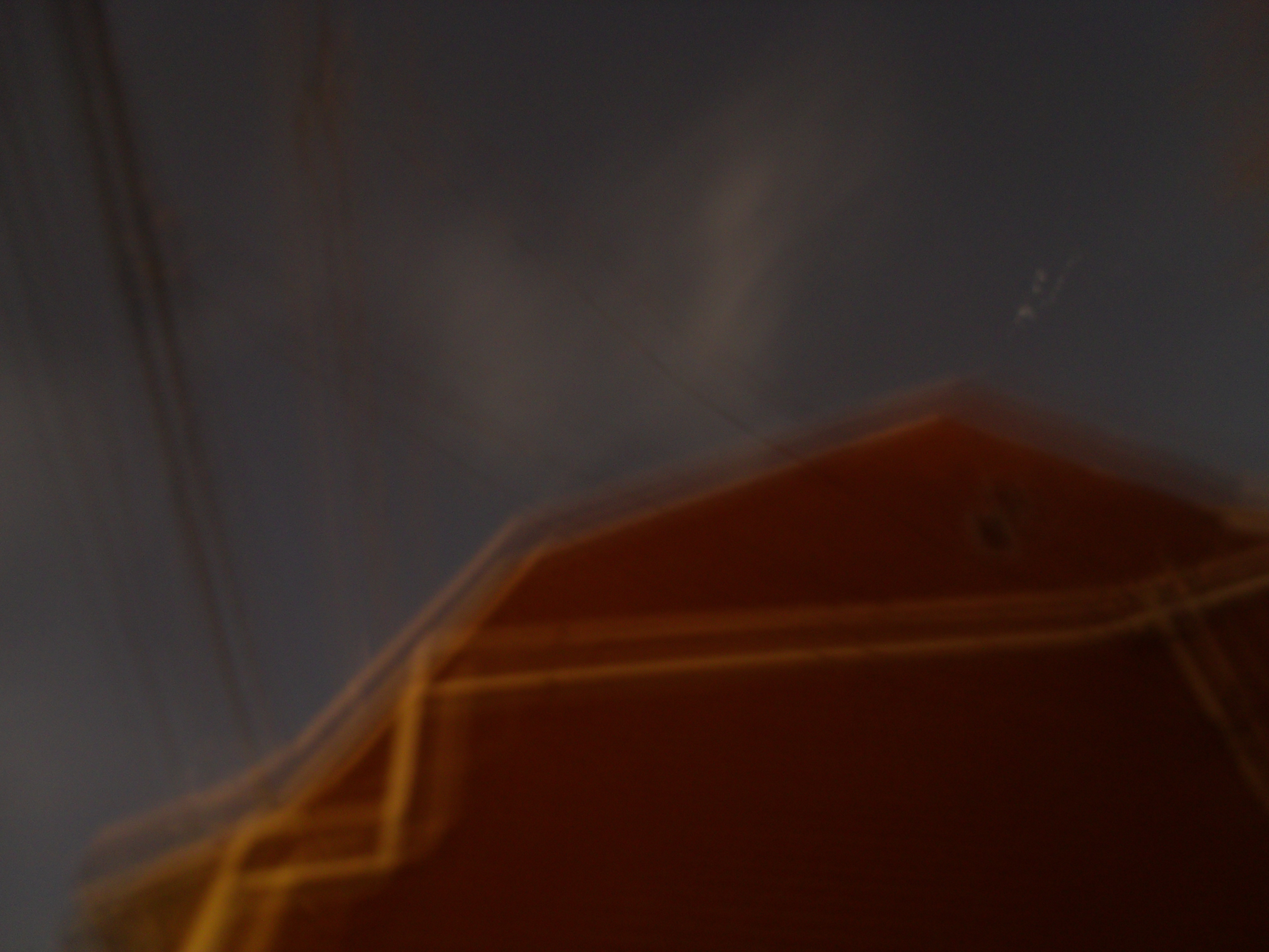 Aurore boréale clairement visible bien que blanchâtre, se déployant comme deux ailes diffuses sur fond de ciel urbain étoilé au-dessus de notre demeure, bâtiment en brique rouge