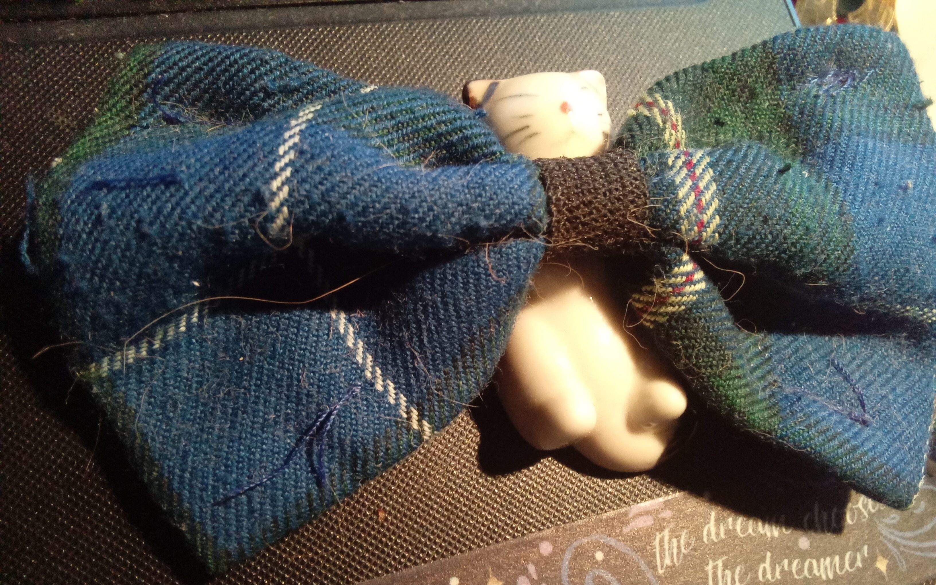 Le noeud papillon bleu carrelé de blanc et vert que Clément le chat a porté quelque temps, maintenant déposé sur une figure de chat plus petite que le noeud papillon.