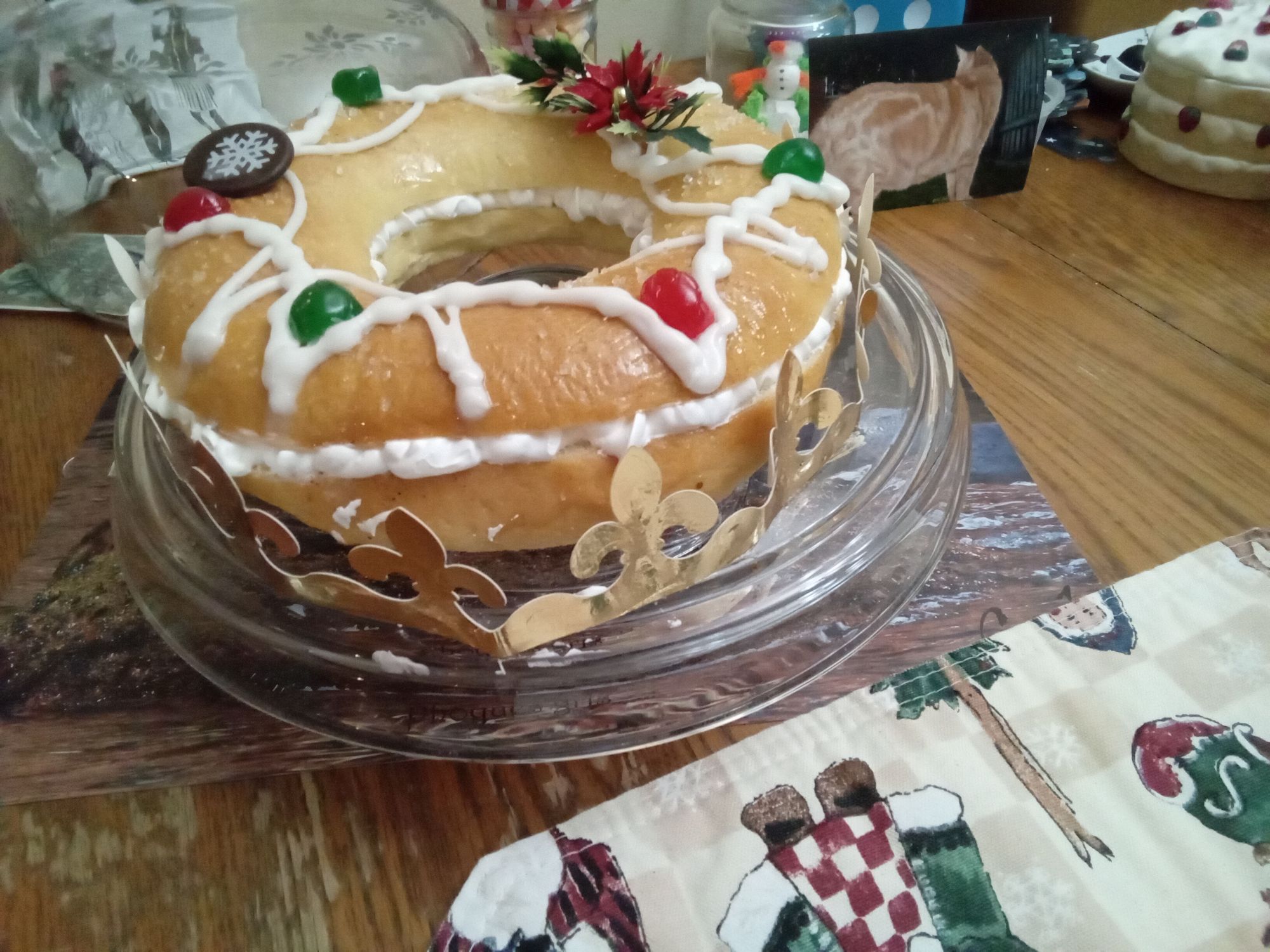Une couronne briochée décorée, remplie de crème à la vanille, et encerclée d'une couronne dorée en papier trône sur la table en avant-plan. En arrière-plan, une photo de Clément de profil.