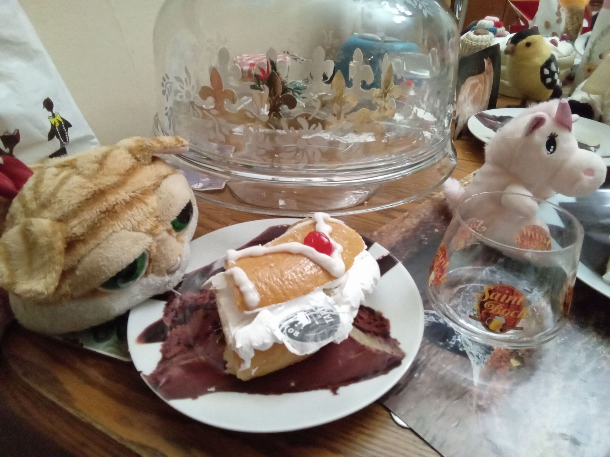 La peluche Clément II, jumeau de Clément le chat, est étendu devant une part de la couronne des rois briochées, "une fève" ou jeton plastifié dépassant de la crème. Iconiki la peluche licorne est assis devant une autre assiette et tout en arrière-plan, une photo de Clément le premier du nom.